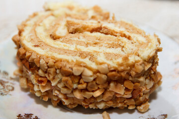 Close-up of a nut-coated sponge cake roll slice on a white plate with floral decor