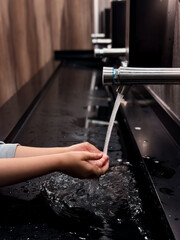 Child washing hands under modern faucet in public restroom