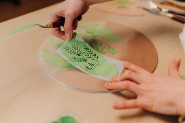 Artist using stencil and palette knife creating fern design on wooden surface