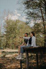Fototapeta premium A couple relaxing during the day in a forest by a lake, with a campfire and hammock, surrounded by nature.