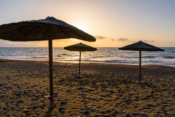 Straw beach umbrellas against background of sunset sky convey atmosphere of rest, romance, peace, end of warm day by sea.