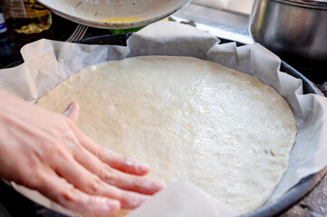 Close-up scene of female hands applying white sauce to dough on kitchen countertop. Making homemade pizza with three types of cheese - female hands in action.