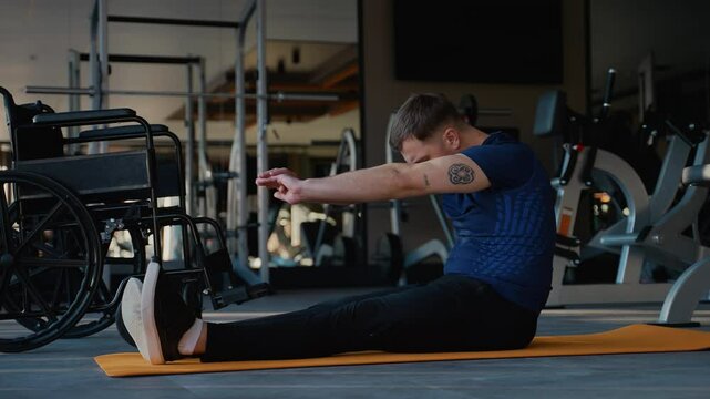 Man with disability doing seated forward stretch on gym mat