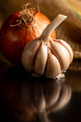 Garlic and onion, a head of garlic and an onion on a black reflective surface and dark background, selective focus.