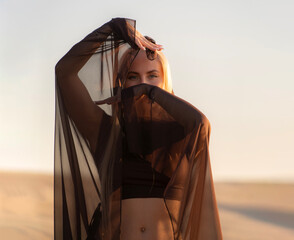 Woman in Traditional Clothing Gracefully Covers Her Face While Posing in a Serene Desert Landscape...