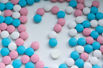 White, blue and pink pills in the shape of a question mark are scattered on the table
