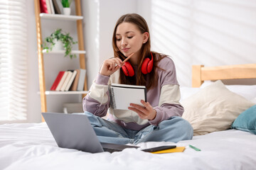 Teenage girl doing homework near laptop on bed at home