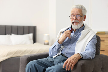 Fototapeta premium Handsome bearded man with tobacco pipe in armchair indoors