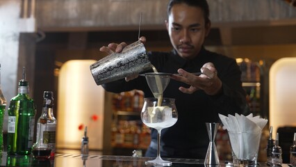 Asian bartender using strainer all ingredients alcohol liquor and syrup tasty in cocktail glass with ice serving special refresh drink showcasing nightlife mixology at luxurious nightclub. Vinosity.