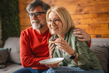 elderly man sit on sofa and watch television woman eat donuts