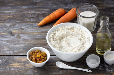 Set of ingredients for carrot cake on rustic wooden table: flour, sugar, carrots, raisins, oil. Home baking, cooking concept, natural ingredients