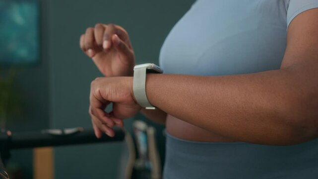 Slowmo of plus-sized Black woman in athletic wear checking her smartwatch after completing her treadmill session, tracking her workout data and fitness goals