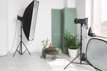 Interior of photo studio with professional equipment, folding screen, pouf and houseplant