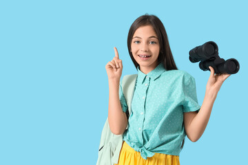 Cute little tourist with binoculars pointing at something on blue background