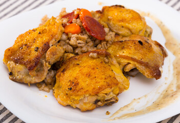 Appetizing fried chicken thighs with pearl barley and braised vegetables on white plate..