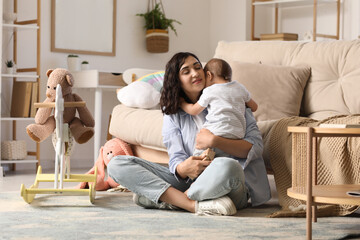 Fototapeta premium Beautiful young happy mother hugging her cute little baby with different toys at home