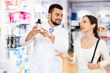 Obraz premium Pharmacist advises customer in a pharmacy, offers medicine for body care
