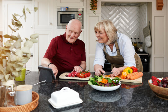 Home, cooking and senior couple with a tablet, smile and digital app with instructions, vegetables and internet. Kitchen, elderly man and old woman with technology, online recipe and healthy food
