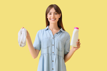 Young woman with dirty socks and laundry detergent on yellow background