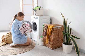 Shocked young woman putting stained t-shirt into washing machine in laundry room