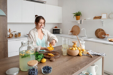 Young woman squeezing lemon for lemonade in kitchen
