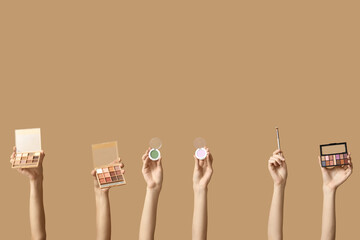 Female hands with different palettes of eyeshadows and makeup brush on brown background