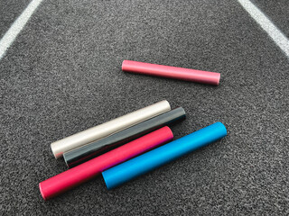 Relay Batons on a Running Track. Multi-colored aluminum relay batons rest on a black running track...