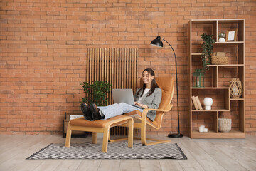 Young woman sitting in armchair and using laptop at home