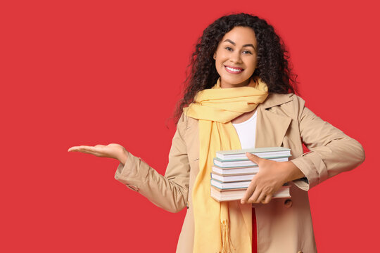 Young African-American woman with books showing something on red background