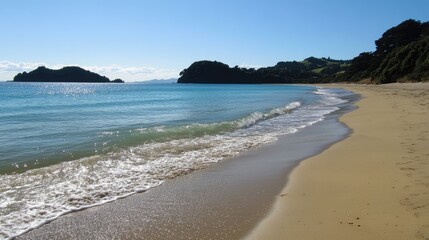 Obraz premium Serene beach with golden sand, gentle waves lapping the shore under a clear blue sky