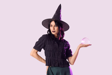 Beautiful young woman dressed as witch for Halloween with crystal ball on lilac background