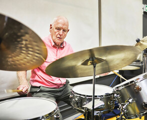 Senior man playing the drums in a music studio for recording a song, track or album with percussion. Talent, musical career and elderly male person from Australia with an instrument or equipment.
