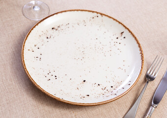 In eating-house on cloth tablecloth, round plate with cutlery, knife and fork complemented by transparent glass for drinks. Restaurant serving option