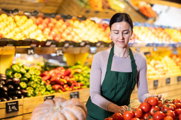 Supermarket employee carefully places ripe tomatoes on shelves of a grocery supermarket