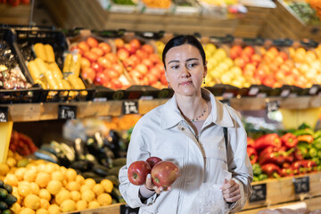 Portrait of female shopper carefully selecting ripe apples on a supermarket display