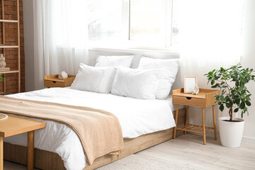 Interior of light bedroom with cozy bed and houseplant near window