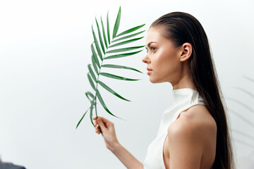 Fototapeta premium Elegant model holding a green palm leaf in a minimalist setting, showcasing a serene expression and modern fashion style.
