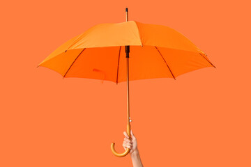 Female hand with orange umbrella on orange background