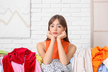 Beautiful young woman with different scattered clothes in messy room