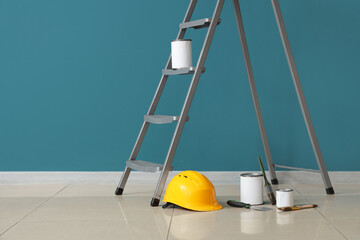 Stepladder with cans of paint, brushes and hardhat near blue wall