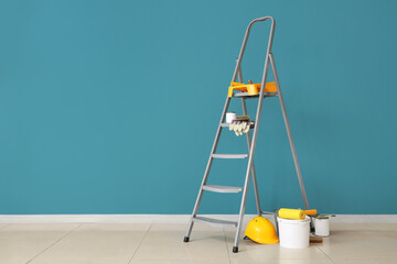 Stepladder with cans of paint and tools near blue wall