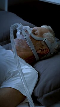 Mature adult sleeping at night while wearing a CPAP mask to treat his Sleep Apnea. Vertical Video.