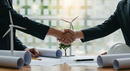 Entrepreneurship, startup, corporate business handshake over blueprints with wind turbine models representing renewable energy project deal