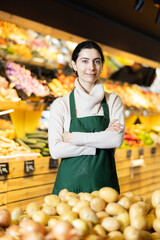 Young woman seller in apron offers potatoes in vegetable shop