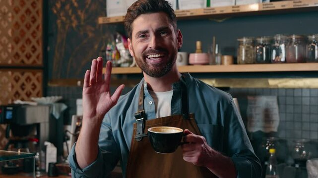 Cheerful Caucasian guy barista male gesturing smiling man waving hand in restaurant bartender greeting symbol small business worker waiter serving carefree employee hold coffee mug order cafe service