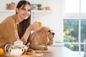 Beautiful young happy woman and cute Cocker Spaniel dog with cup of green tea in kitchen at home