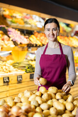 Supermarket female worker inspects vegetables, checks the quality of potatoes, rearranges products and sets up a display case