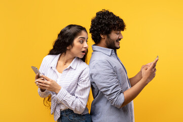 Shocked indian woman spying on her smiling boyfriend who using smartphone, chatting or scrolling...