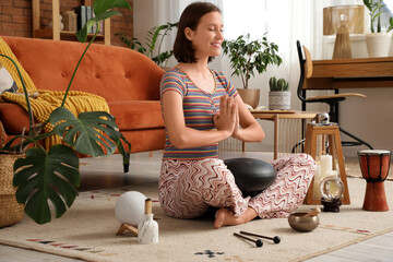 Young woman with glucophone meditating on carpet at home