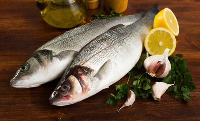 Uncooked sea bass fish with lemon and greens on wooden board